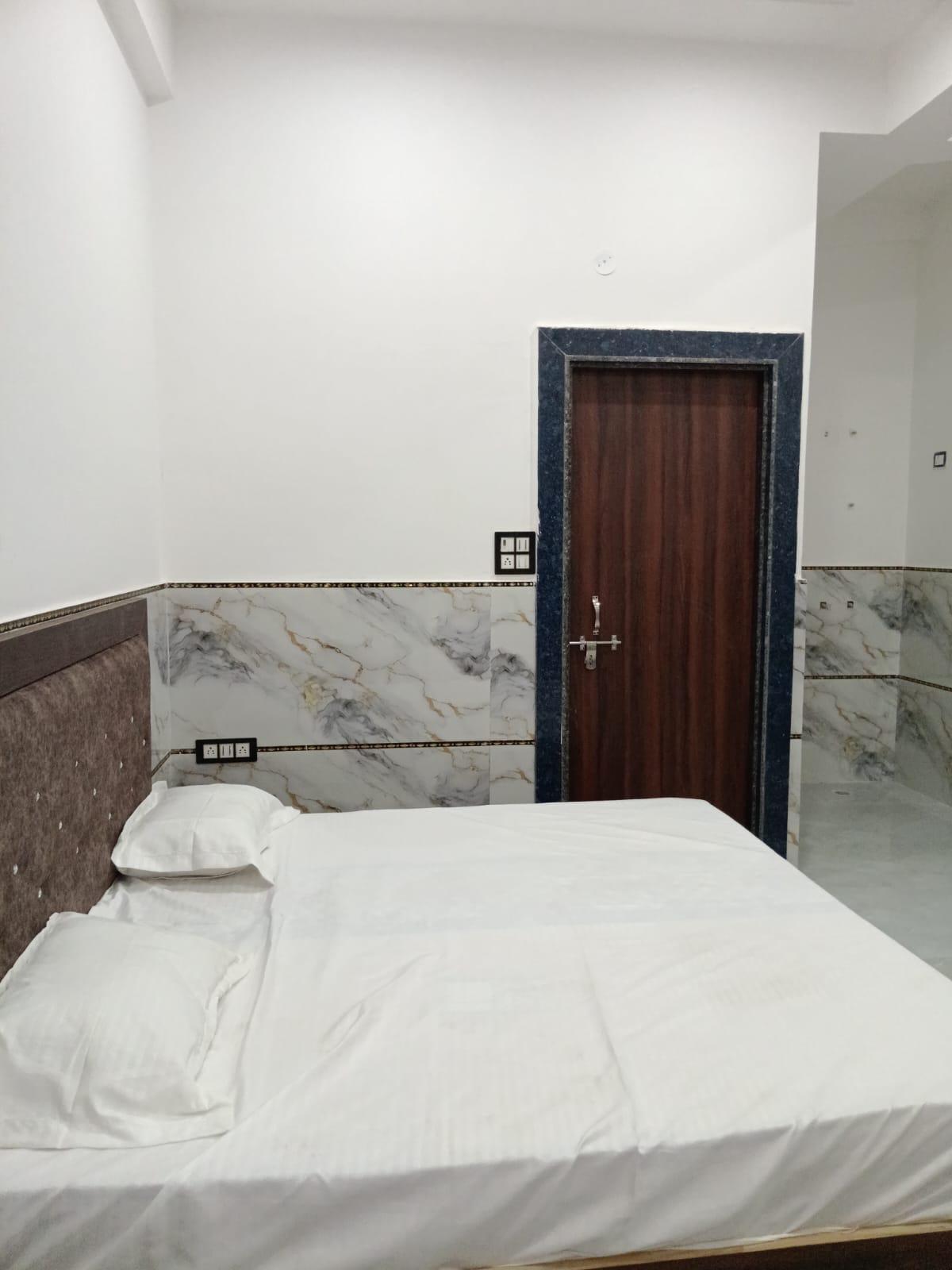 Bed with white linen, marble-finish tiled walls and a wooden door